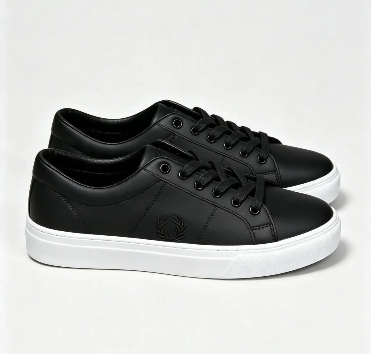 These appear to be black leather Fred Perry tennis sneakers featuring a lace-up front and the brand's signature embroidered laurel wreath logo on the side.