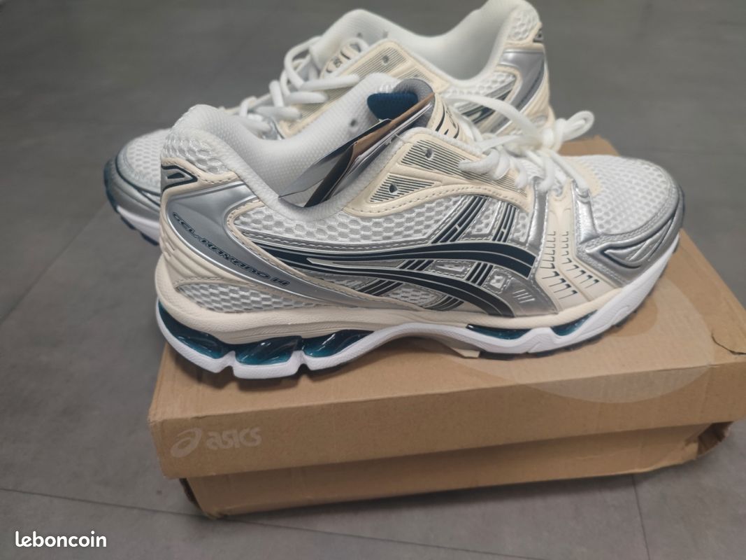 The sneaker shown in the image is the ASICS Gel-Kayano 14, featuring a design inspired by the late 2000s with white and silver BLUE mesh overlays.