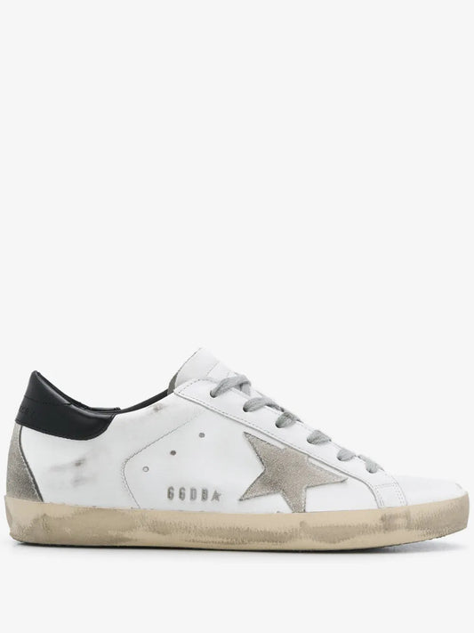 The image shows a pair of Golden Goose "Ball Star" sneakers, crafted from white leather with black details and a star, featuring a distressed effect inspired by 1980s style.